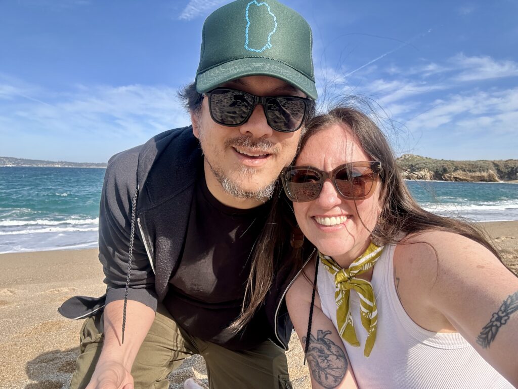 Nicki and Yonas wear sunglasses and smile at the camera at the beach