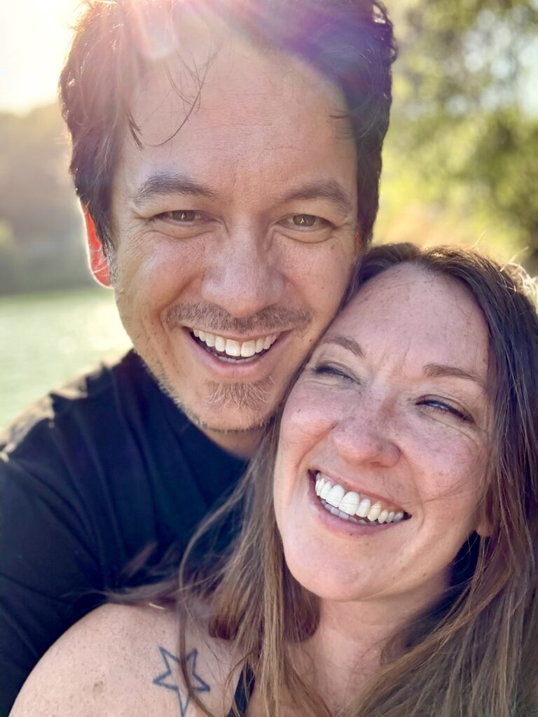 Nicki and Yonas are smiling at the camera, behind them is a lake